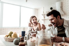 Hombre positivo hermoso barbudo en una camisa blanca que come desayunando con su esposa fotografía de archivo Hombre positivo hermoso barbudo en una camisa blanca que come desayunando con su esposa fotografía de archivo