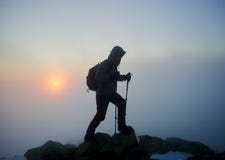 Hombre turístico del caminante con la mochila en la montaña rocosa en el cielo azul brumoso y el aumento del fondo del sol imagenes de archivo Hombre turístico del caminante con la mochila en la montaña rocosa en el cielo azul brumoso y el aumento del fondo del sol imagenes de archivo