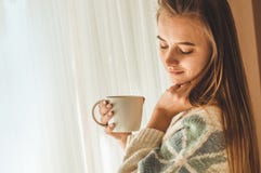 HOME acolhedor Mulher com o copo da bebida quente pela janela Olhando o chá da janela e da bebida bom dia com chá Rapariga que re fotos de stock HOME acolhedor Mulher com o copo da bebida quente pela janela Olhando o chá da janela e da bebida bom dia com chá Rapariga que re fotos de stock
