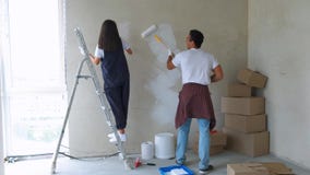 Home makeover and renovation: young happy couple painting their new house interiors using paint rollers stock video footage Home makeover and renovation: young happy couple painting their new house interiors using paint rollers stock video footage