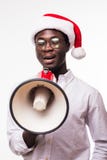 Homem afro-americano novo que veste um chapéu de Santa com o altifalante isolado no fundo branco foto de stock royalty free Homem afro-americano novo que veste um chapéu de Santa com o altifalante isolado no fundo branco foto de stock royalty free
