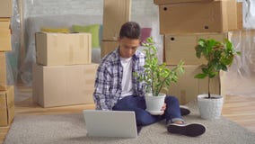 Homem asiático novo após mover-se para um apartamento novo que senta-se em um portátil no assoalho filme Homem asiático novo após mover-se para um apartamento novo que senta-se em um portátil no assoalho filme