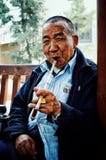 Homem chinês que fuma uma tubulação longa com um charuto calmamente durante o calor da tarde foto de stock Homem chinês que fuma uma tubulação longa com um charuto calmamente durante o calor da tarde foto de stock