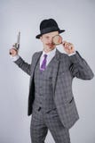 Homem com um bigode vestido em um terno da manta do negócio com um laço, retendo uma lupa e uma arma em um estúdio contínuo branc fotografia de stock royalty free Homem com um bigode vestido em um terno da manta do negócio com um laço, retendo uma lupa e uma arma em um estúdio contínuo branc fotografia de stock royalty free