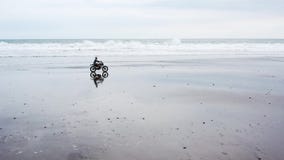 Homem consider?vel novo do moderno que monta o piloto feito sob encomenda moderno da motocicleta na praia preta da areia perto da video estoque Homem consider?vel novo do moderno que monta o piloto feito sob encomenda moderno da motocicleta na praia preta da areia perto da video estoque