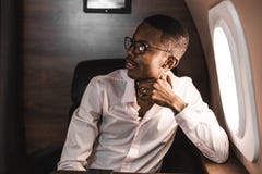 Homem de neg?cios preto afro-americano novo bem sucedido que senta-se na cadeira de seu jato privado fotos de stock royalty free Homem de neg?cios preto afro-americano novo bem sucedido que senta-se na cadeira de seu jato privado fotos de stock royalty free