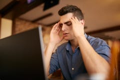 Homem de negócios frustrante sério com os olhos fechados que sofrem da enxaqueca da dor de cabeça no local de trabalho, fazendo m fotografia de stock Homem de negócios frustrante sério com os olhos fechados que sofrem da enxaqueca da dor de cabeça no local de trabalho, fazendo m fotografia de stock