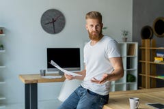 Homem de negócios novo farpado que trabalha no escritório moderno Equipe o t-shirt branco vestindo e notas da fatura nos originai Imagem de Stock Royalty Free Homem de negócios novo farpado que trabalha no escritório moderno Equipe o t-shirt branco vestindo e notas da fatura nos originai Imagem de Stock Royalty Free