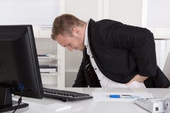 Homem de negócios que senta-se na mesa que tem a dor na parte traseira, nos rins ou no musc imagens de stock royalty free Homem de negócios que senta-se na mesa que tem a dor na parte traseira, nos rins ou no musc imagens de stock royalty free