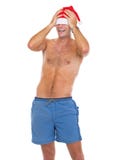 Homem de sorriso no short da praia que puxa o chapéu de Santa sobre os olhos fotografia de stock royalty free Homem de sorriso no short da praia que puxa o chapéu de Santa sobre os olhos fotografia de stock royalty free