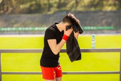 Homem desportivo novo que descansa e que limpa seu suor com uma toalha ap?s exerc?cios do esporte do exerc?cio fora fotografia de stock royalty free Homem desportivo novo que descansa e que limpa seu suor com uma toalha ap?s exerc?cios do esporte do exerc?cio fora fotografia de stock royalty free