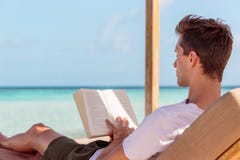 Homem em um sunchair que lê um livro em um lugar tropical ?gua clara de turquesa como o fundo foto de stock royalty free Homem em um sunchair que lê um livro em um lugar tropical ?gua clara de turquesa como o fundo foto de stock royalty free