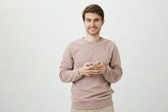 Homem encantador satisfeito com a cerda que guarda o smartphone perto da caixa, sorrindo e olhando a câmera, estando sobre o cinz fotos de stock Homem encantador satisfeito com a cerda que guarda o smartphone perto da caixa, sorrindo e olhando a câmera, estando sobre o cinz fotos de stock