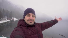 Homem feliz do viajante que toma o selfie e que mostra o lago Ritsa na Abkhásia Dia nevado no inverno video estoque Homem feliz do viajante que toma o selfie e que mostra o lago Ritsa na Abkhásia Dia nevado no inverno video estoque