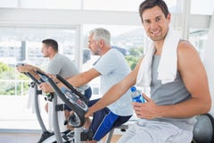 Homem na bicicleta de exercício que guarda a garrafa de água foto de stock royalty free Homem na bicicleta de exercício que guarda a garrafa de água foto de stock royalty free
