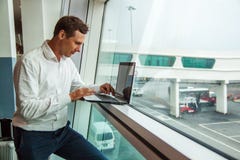 Homem novo considerável que trabalha com o portátil no aeroporto ao esperar seu plano fotos de stock royalty free Homem novo considerável que trabalha com o portátil no aeroporto ao esperar seu plano fotos de stock royalty free