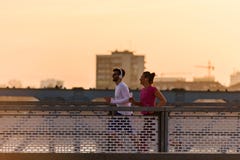 Homem novo e mulher que movimentam-se junto sobre a ponte no por do sol ou no nascer do sol imagens de stock Homem novo e mulher que movimentam-se junto sobre a ponte no por do sol ou no nascer do sol imagens de stock