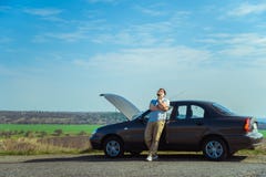 Homem novo irritado que espera uma ajuda ao sentar-se perto do carro quebrado foto de stock Homem novo irritado que espera uma ajuda ao sentar-se perto do carro quebrado foto de stock
