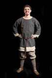 Homem novo na roupa cinzenta ocasional e em um chapéu dos sorrisos adiantados da Idade Média de Viking Age fotografia de stock Homem novo na roupa cinzenta ocasional e em um chapéu dos sorrisos adiantados da Idade Média de Viking Age fotografia de stock