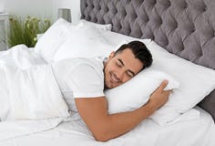 Homem novo que dorme na cama com descansos macios imagem de stock royalty free Homem novo que dorme na cama com descansos macios imagem de stock royalty free
