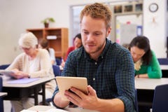 Homem novo que usa o tablet pc em uma classe do ensino para adultos imagem de stock Homem novo que usa o tablet pc em uma classe do ensino para adultos imagem de stock
