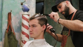 Homem novo sério do moderno que obtém o corte de cabelo pelo barbeiro profissional no barbeiro Posição e fatura farpadas novas do video estoque Homem novo sério do moderno que obtém o corte de cabelo pelo barbeiro profissional no barbeiro Posição e fatura farpadas novas do video estoque