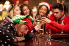 Homem passado para fora na barra durante bebidas do Natal com amigos imagem de stock Homem passado para fora na barra durante bebidas do Natal com amigos imagem de stock