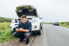 Homem que senta-se perto de carro quebrado com o telefone, procurando a ajuda imagem de stock royalty free Homem que senta-se perto de carro quebrado com o telefone, procurando a ajuda imagem de stock royalty free