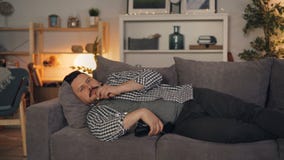Homem sonolento da pessoa que olha a tevê comer a pipoca que encontra-se no sofá em casa apenas video estoque Homem sonolento da pessoa que olha a tevê comer a pipoca que encontra-se no sofá em casa apenas video estoque