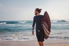 Homem à moda desportivo atrativo novo com uma prancha nas mãos na perspectiva do oceano imagens de stock Homem à moda desportivo atrativo novo com uma prancha nas mãos na perspectiva do oceano imagens de stock
