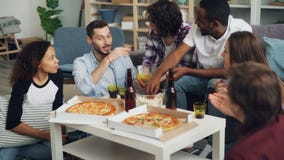 Homens e mulheres dos jovens que comem e que conversam durante o partido interno no apartamento Homens e mulheres dos jovens que comem e que conversam durante o partido interno no apartamento