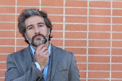 Homme barbu mûr de pensée dans un costume avec toucher sa barbe regardant loin Portrait désaturé au-dessus de fond de mur de briq Photos stock Homme barbu mûr de pensée dans un costume avec toucher sa barbe regardant loin Portrait désaturé au-dessus de fond de mur de briq Photos stock