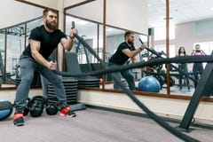 Homme barbu musculaire sportif s'exerçant dans le gymnase avec des cordes de bataille Sport, formation, les gens, concept sain de images stock Homme barbu musculaire sportif s'exerçant dans le gymnase avec des cordes de bataille Sport, formation, les gens, concept sain de images stock