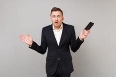 Homme choqué d'affaires dans des mains de propagation de costume noir classique, tenant le téléphone portable avec l'écran vide v photographie stock libre de droits Homme choqué d'affaires dans des mains de propagation de costume noir classique, tenant le téléphone portable avec l'écran vide v photographie stock libre de droits