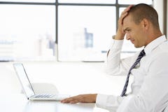 Homme d'affaires frustrant Sitting At Desk dans le bureau utilisant l'ordinateur portable photos stock Homme d'affaires frustrant Sitting At Desk dans le bureau utilisant l'ordinateur portable photos stock