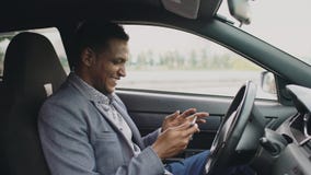 Homme d'affaires heureux d'afro-américain surfant le media social sur sa tablette se reposant à l'intérieur de sa voiture Image stock Homme d'affaires heureux d'afro-américain surfant le media social sur sa tablette se reposant à l'intérieur de sa voiture Image stock