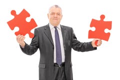 Homme d'affaires mûr tenant deux morceaux d'un puzzle photo stock Homme d'affaires mûr tenant deux morceaux d'un puzzle photo stock