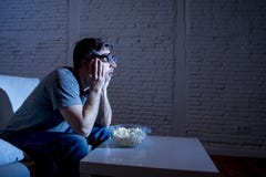 Homme d'intoxiqué de télévision sur le sofa regardant la TV et mangeant du maïs éclaté en verres drôles de connaisseur de ballot photo stock Homme d'intoxiqué de télévision sur le sofa regardant la TV et mangeant du maïs éclaté en verres drôles de connaisseur de ballot photo stock