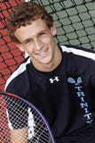 Homme d'une chevelure de Brown jeune souriant avec la raquette de tennis Image stock Homme d'une chevelure de Brown jeune souriant avec la raquette de tennis Image stock