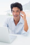 Homme de sourire à l'aide de son ordinateur portable et parlant au téléphone Photographie stock libre de droits