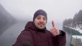 Homme prenant le selfie et montrant le pouce au lac Ritsa en l'Abkhazie en hiver banque de vidéos Homme prenant le selfie et montrant le pouce au lac Ritsa en l'Abkhazie en hiver banque de vidéos