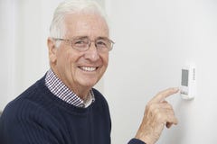 Homme supérieur de sourire ajustant le thermostat de chauffage central photos stock Homme supérieur de sourire ajustant le thermostat de chauffage central photos stock