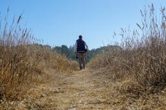 Homme tropical de pluie marchant au-dessus d'un champ dans une veste bleue et le pantalon de kaki photo stock Homme tropical de pluie marchant au-dessus d'un champ dans une veste bleue et le pantalon de kaki photo stock