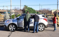 Hommes attachant un arbre de Noël sur SUV tandis qu'une femme les observe dans un sort vivant d'arbre de Noël à Tulsa, l'Oklahoma images stock Hommes attachant un arbre de Noël sur SUV tandis qu'une femme les observe dans un sort vivant d'arbre de Noël à Tulsa, l'Oklahoma images stock