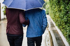 Homosexuelle Paare, die Regenschirm und Hände zusammenhalten Zurück von den homosexuellen Männern, die in den Regen gehen lizenzfreie stockfotos Homosexuelle Paare, die Regenschirm und Hände zusammenhalten Zurück von den homosexuellen Männern, die in den Regen gehen lizenzfreie stockfotos