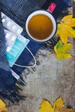 Hoogste mening van een kop thee, een blauwe sjaal, een thermometer, drugs en medische gezichtsmasker en bladeren op houten achter stock afbeelding Hoogste mening van een kop thee, een blauwe sjaal, een thermometer, drugs en medische gezichtsmasker en bladeren op houten achter stock afbeelding