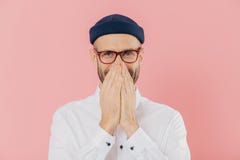 Horizontal shot of positive glad male expresses positive emotions, covers mouth with both hands, giggles silently, wears headgear stock photo Horizontal shot of positive glad male expresses positive emotions, covers mouth with both hands, giggles silently, wears headgear stock photo