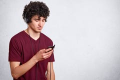 Horizontal shot of young handsome man, has dark curly hair, guy with cell phone in hand and earphones listening to music on white royalty free stock image Horizontal shot of young handsome man, has dark curly hair, guy with cell phone in hand and earphones listening to music on white royalty free stock image