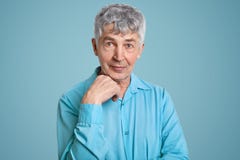 Horizontaler Schuss des reifen grauen behaarten kaukasischen männlichen Pensionärs trägt elegantes Hemd, hält Hand unter Kinn, au lizenzfreie stockfotos Horizontaler Schuss des reifen grauen behaarten kaukasischen männlichen Pensionärs trägt elegantes Hemd, hält Hand unter Kinn, au lizenzfreie stockfotos