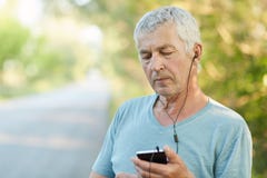 Horyzontalny strzał przystojny popielaty z włosami męski emeryt słucha radio z słuchawkami i smartphone, używa bezprzewodowego in obraz stock Horyzontalny strzał przystojny popielaty z włosami męski emeryt słucha radio z słuchawkami i smartphone, używa bezprzewodowego in obraz stock